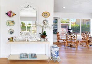 Un coin repas avec une console blanche, des assiettes décoratives, un vase avec des fleurs blanches et des chaises en osier.