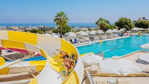 A water slide at a resort with a pool and umbrellas in the background. - Louis St. Elias Resort & Waterpark (Paralimni)