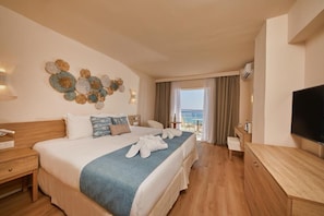 Habitación de hotel con cama, mesita de noche, televisor y vista al mar a través de un ventanal grande.