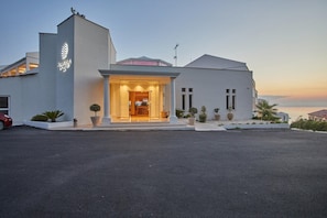Un hotel moderno con una entrada destacada, vista despejada al mar y un área exterior bien cuidada con plantas en macetas.
