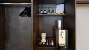 Une petite cuisine équipée comprenant une machine à café, des dosettes de thé et de café, un porte-verres à vin et une petite étagère avec une bouteille.