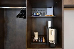 Eine kompakte Küchenzeile mit Kaffeemaschine, Kaffeekapseln, Tee, einem Weinglashalter und einem kleinen Regal mit einer Flasche.