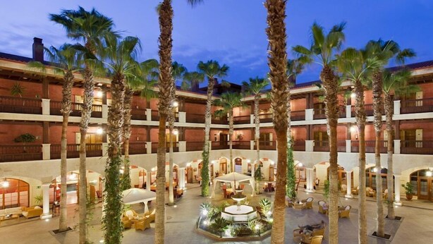 A multi-story hotel atrium with palm trees, outdoor seating, and a central fountain. - Elba Palace Golf Boutique Hotel (Antigua)