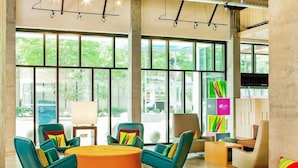 A modern lounge area with large windows, colorful chairs, and a central ottoman. - Aloft Atlanta Downtown (Atlanta)