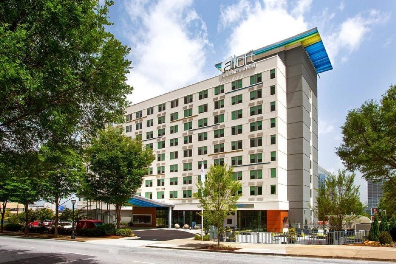 A modern hotel with a flat roof, multiple floors, and a prominent logo on the top.