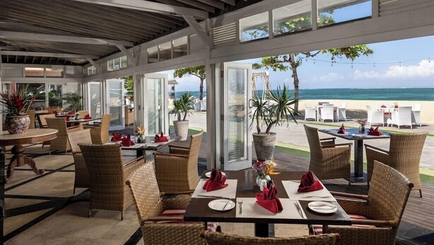 Un espace de restauration en plein air, doté de mobilier et de tables en osier, aménagé pour les repas et offrant une vue sur la plage.