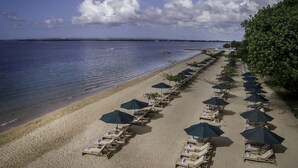 Une plage bordée de rangées de transats et de parasols, un rivage sablonneux et une mer calme.