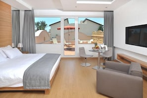 Une chambre d’hôtel moderne dotée d’un grand lit, d’un petit bureau, d’une télévision et d’un balcon avec coin salon extérieur.