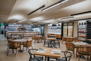 A modern restaurant with wooden tables and chairs, a central bar area, and shelves with bottles and glasses. - Napa Plaza Hotel-adults Only (AYIA NAPA)