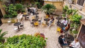 An outdoor patio with stone flooring, multiple tables and chairs, and lush greenery.