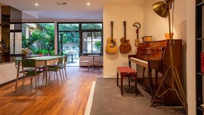 A spacious living room with a piano, a dining table with chairs, and a large window offering a view of greenery outside. - Hotel Edera (Rome)
