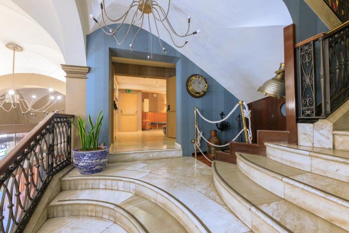 Una imponente escalera de mármol conduce a un segundo piso, con un candelabro y una planta en maceta.
