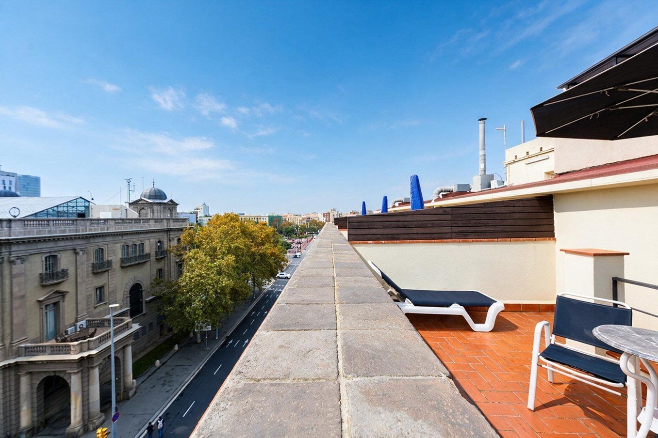 Una terraza en la azotea con vistas despejadas de la ciudad, un espacio de descanso y un edificio moderno al fondo.