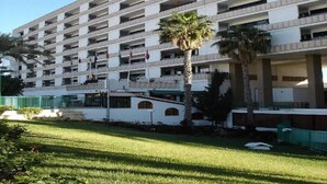 A multi-story hotel with balconies, palm trees, and a grassy courtyard. - Koka Apartamentos (San Bartolomé de Tirajana)