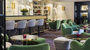 Un espace bar doté de chaises à revêtement vert, d’un comptoir en marbre et de statues décoratives.