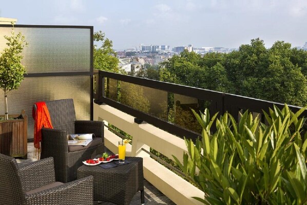 A balcony with wicker furniture, a table with a drink, and a city view. - Hotel Barsey by Warwick (Brussels)