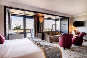 A hotel room with a large bed, a sofa, two armchairs, a TV, and a view of the city. - Hotel Barsey by Warwick (Brussels)