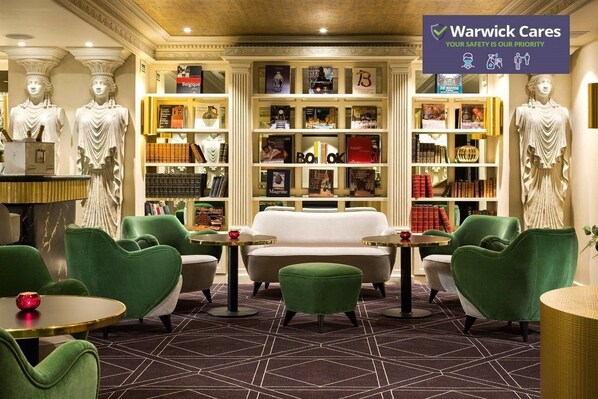 Een bibliotheek met boekenplanken, een witte bank, groene fauteuils en een marmeren vloer.