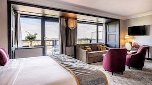 Une chambre d’hôtel avec un grand lit, un canapé, deux fauteuils, une télévision et une vue sur la ville.