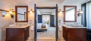 A hotel bathroom with two sinks, a mirror, a towel rack, and a door leading to a bedroom. - Hotel Barsey by Warwick (Brussels)