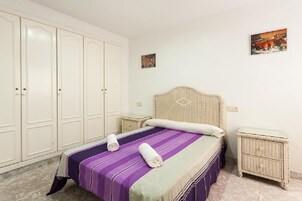 Un dormitorio con una cama, dos mesitas de noche, un cabecero y un armario.