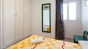 Un dormitorio con cama, armario, espejo, ventana y cortinas.