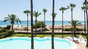 Zona de piscina con palmeras, playa y cielo despejado.