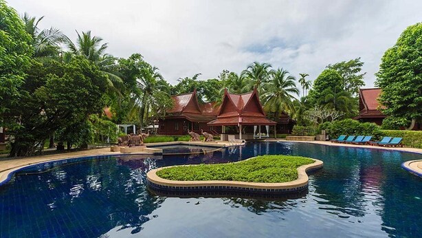Ein Resort mit großem Pool, Palmen und Gebäuden im traditionellen Stil.
