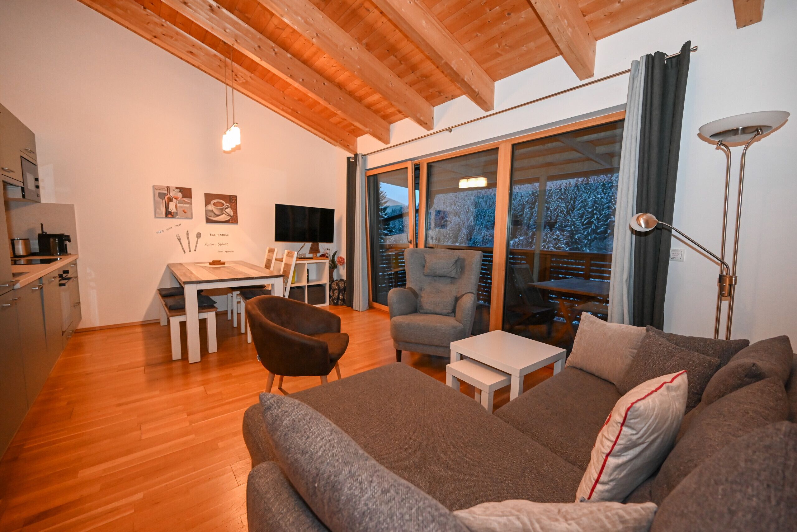 A modern living room with a sofa, armchairs, a dining table, and a kitchen area.