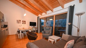 A modern living room with a sofa, armchairs, a dining table, and a kitchen area. - Schmitten Finest Apartment - LEO (Zell am See)