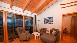 A cozy living room with a sofa, armchair, and a small table. There is a sliding glass door leading to a balcony. - Schmitten Finest Apartment - LEO (Zell am See)