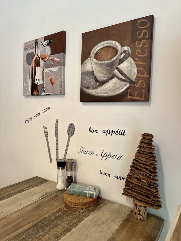 A wall with two framed artworks depicting a bottle and a cup, and a text saying 'bon appétit' in multiple languages.