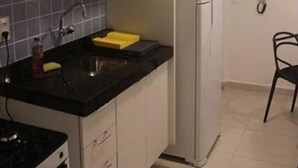 A compact kitchen with white cabinets, a black countertop, a stainless steel refrigerator, and a tiled backsplash. - CPG02 Flat Piscina Privada em Porto (Ipojuca)