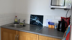 Une cuisine dotée de meubles en bois, d’un plan de travail en granit, d’un four à micro-ondes, d’une bouilloire et d’un évier.