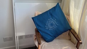 Une chaise avec un coussin bleu et un autre coussin à motifs, un radiateur blanc et une prise de courant sur le mur.