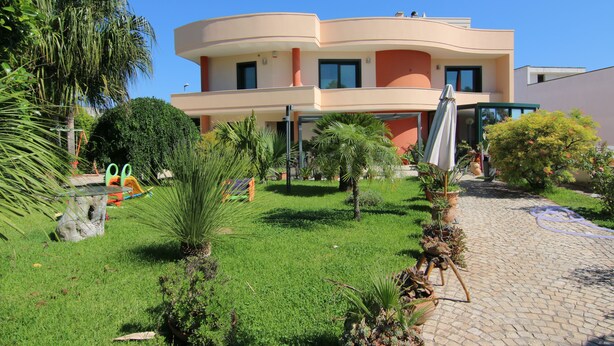 A modern two-story building with a curved facade, surrounded by well-maintained greenery and a paved pathway. - B & B Paradise (Melendugno)