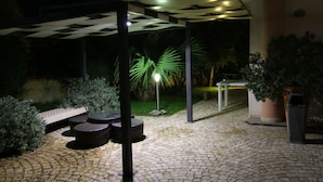 A nighttime outdoor area with a paved walkway, seating, and a palm tree illuminated by a light. - B & B Paradise (Melendugno)