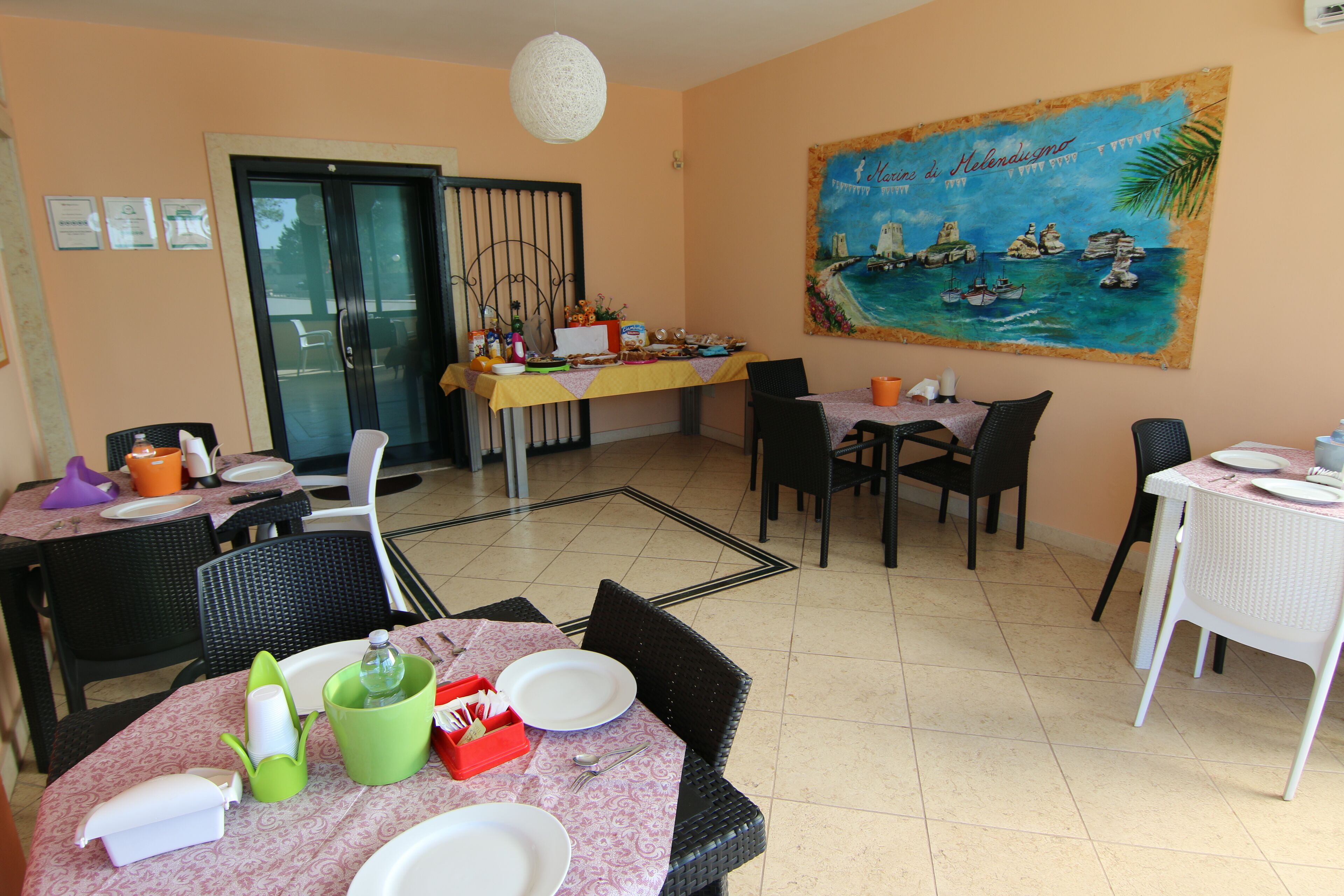 A dining area with tables set for meals, chairs, and a painting of a coastal scene on the wall.