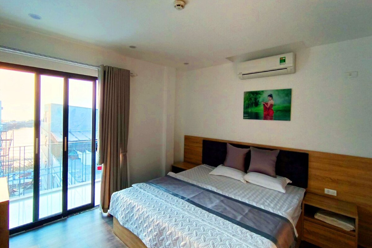 A hotel room with a large bed, a sliding glass door to a balcony, and an air conditioning unit on the wall.