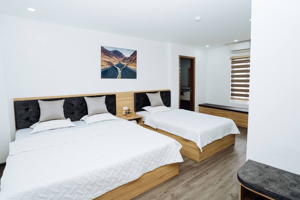 A hotel room with two beds, a wooden headboard, a painting on the wall, and a window with blinds.