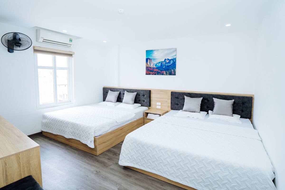 A hotel room with two beds, a window, an air conditioner, and a painting on the wall.