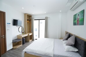 A modern hotel room with a large bed, a TV mounted on the wall, a wooden wardrobe, and a balcony with curtains. - Thanh Mang Hotel (Co To)