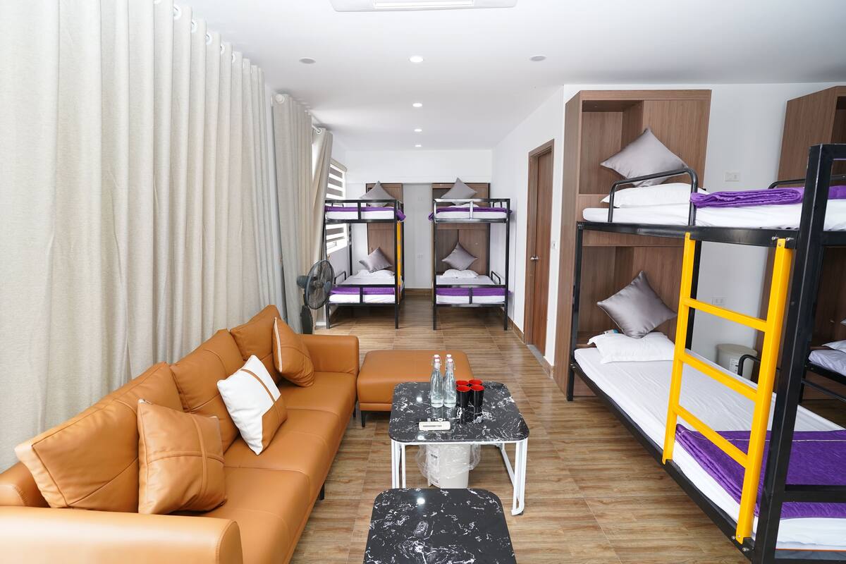 A hotel room with a sofa, a small table, bunk beds, and a fan.