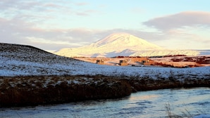 Paesaggio innevato con un fiume, una montagna sullo sfondo e un piccolo edificio con il tetto rosso.