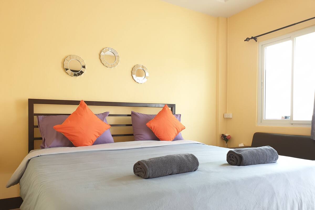 A hotel room with a bed, pillows, a window, and wall decor.