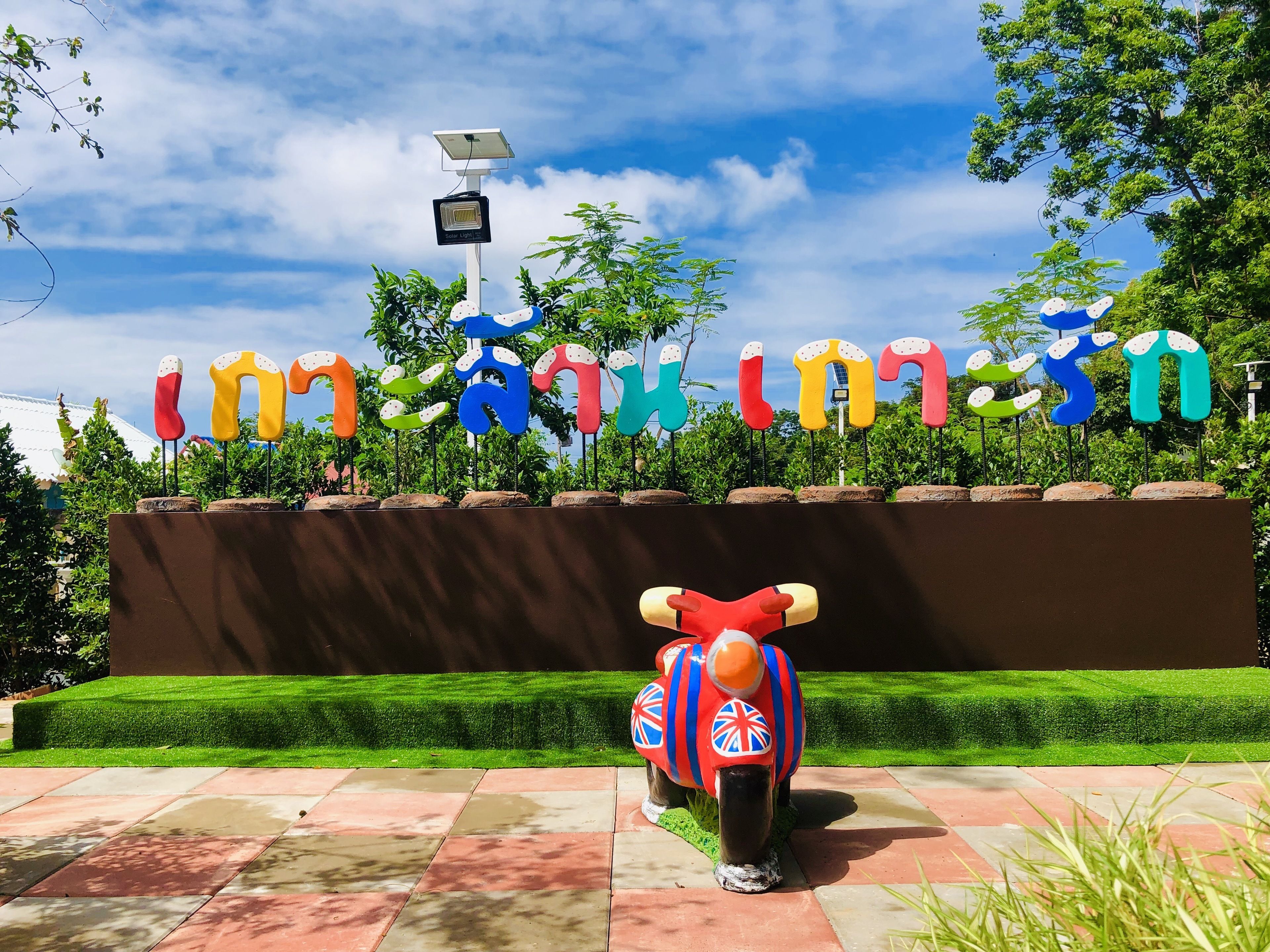 A colorful sign with Thai characters, a solar-powered light, and a red elephant statue with Union Jack decorations.