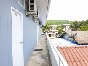A narrow corridor with a door labeled '14', air conditioning units, and a view of neighboring houses with a green landscape in the background.