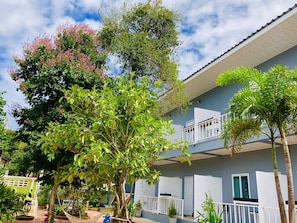 A multi-story building with balconies, surrounded by lush greenery and trees.