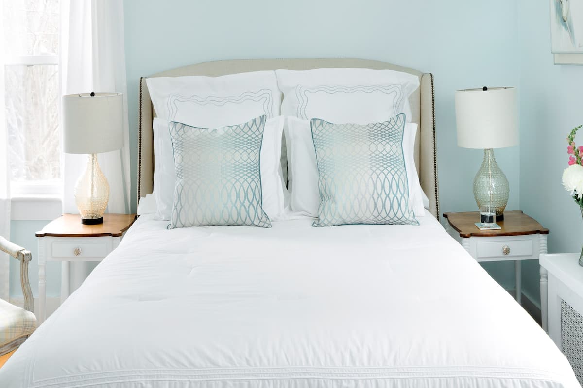 A neatly arranged bedroom with a large bed, two bedside tables with lamps, a chair, and a window with curtains.