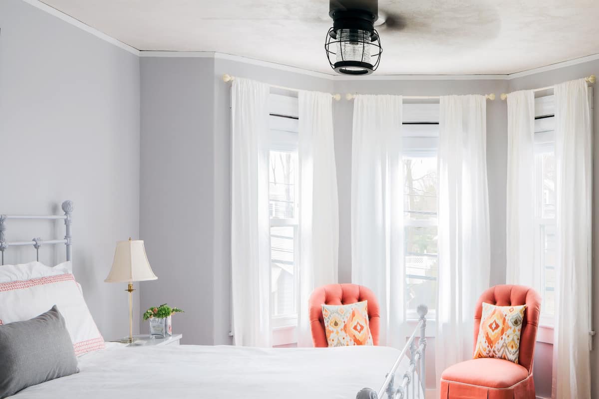 A bedroom with a large bed, two chairs, a nightstand, and a lamp.